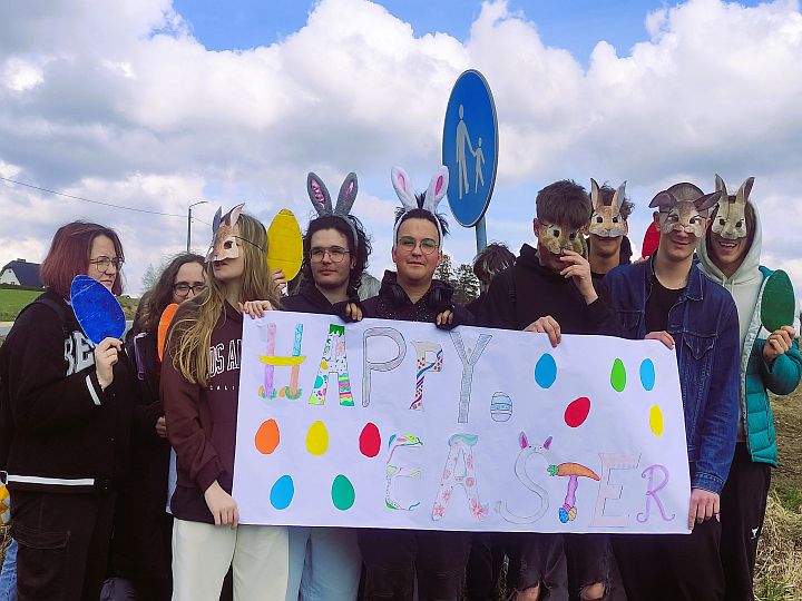 Grupa uczniów w plenerze wraz z nauczycielem, w rękach trzymają duży napis Happy Easter