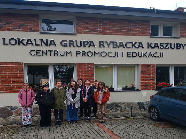 Grupa uczniów przed budynkiem, na którym znajduje się napis Lokalna Grupa Rybacka - Centrum Promocji i Edukacji